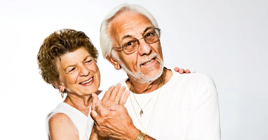 Siwy mężczyzna trzyma rękę uśmiechniętej kobiety w podeszłym wieku