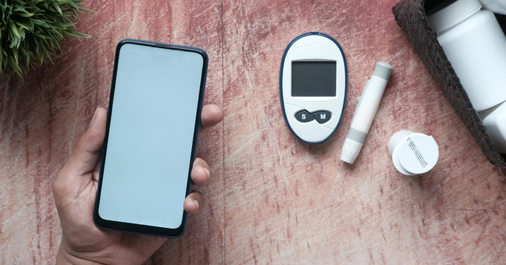 Ręka trzymająca smartfon oraz obok leżący glukometr