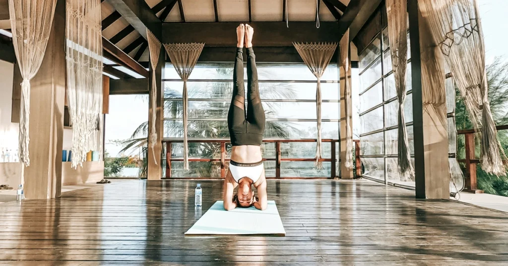 Kobieta stoi na głowie w jasnym przeszklonym pomieszczeniu