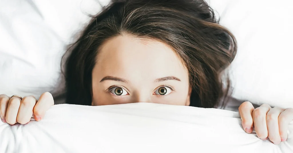 Przestraszona kobieta zakrywa połowę twarzy kołdrą