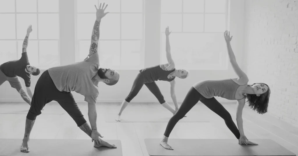 Grupa osób wykonuje trójkąt (trikonasana)